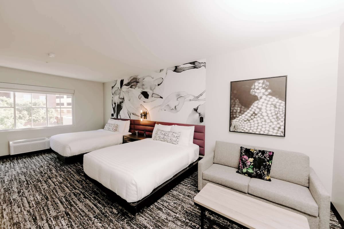 Une chambre d’hôtel avec deux lits, un canapé, une grande peinture abstraite et un tableau encadré accroché au mur.