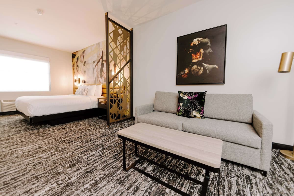 Une chambre d’hôtel comprenant un lit, un canapé, une table basse, un paravent décoratif et un tableau au mur.