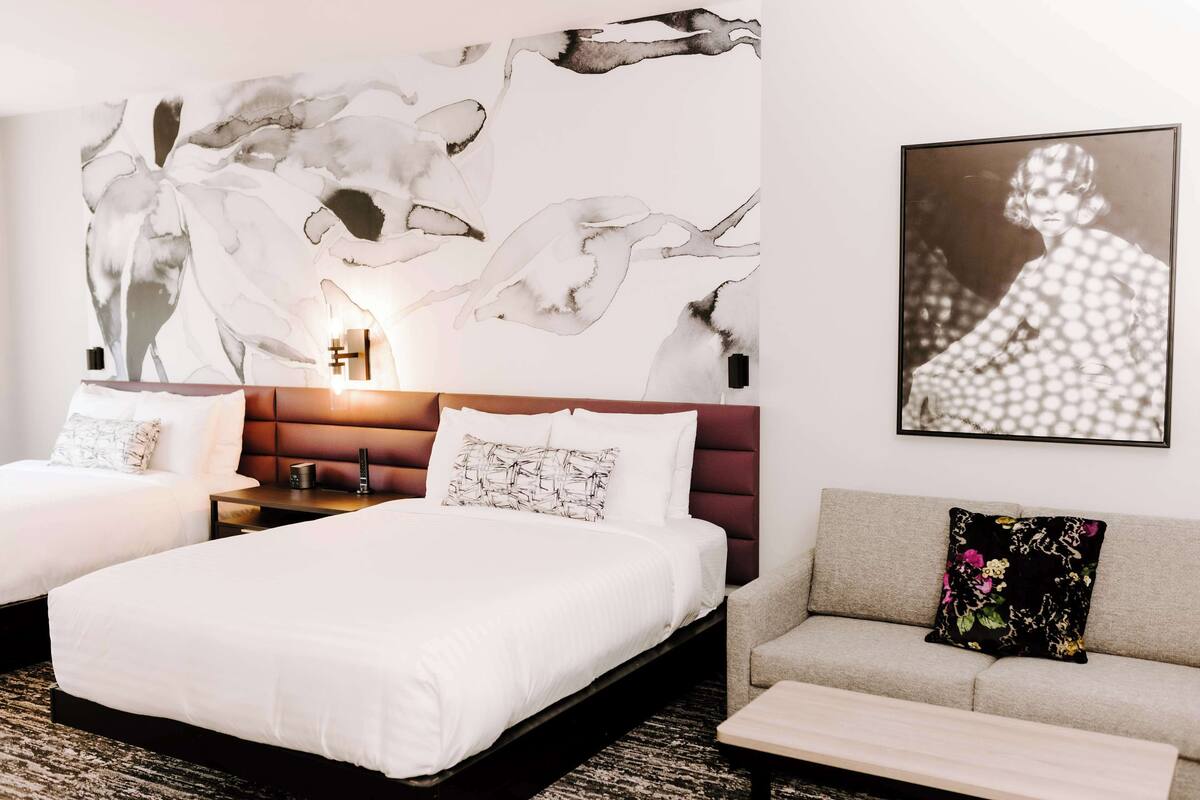 Une chambre d’hôtel avec deux lits, un canapé, un grand tableau abstrait et une photographie encadrée accrochée au mur.