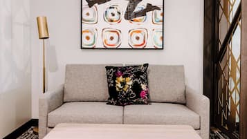 A modern living room with a grey sofa, a black floral pillow, and a large abstract painting on the wall.