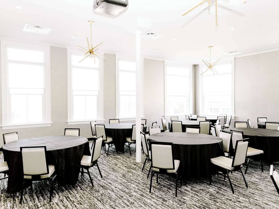 Un salón de conferencias con varias mesas redondas y sillas, ventanas amplias y luminarias modernas.