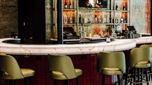 A bar area with a marble countertop, green bar stools, and shelves with bottles and a television displaying a fire. -  Aiden San Antonio Riverwalk (San Antonio)