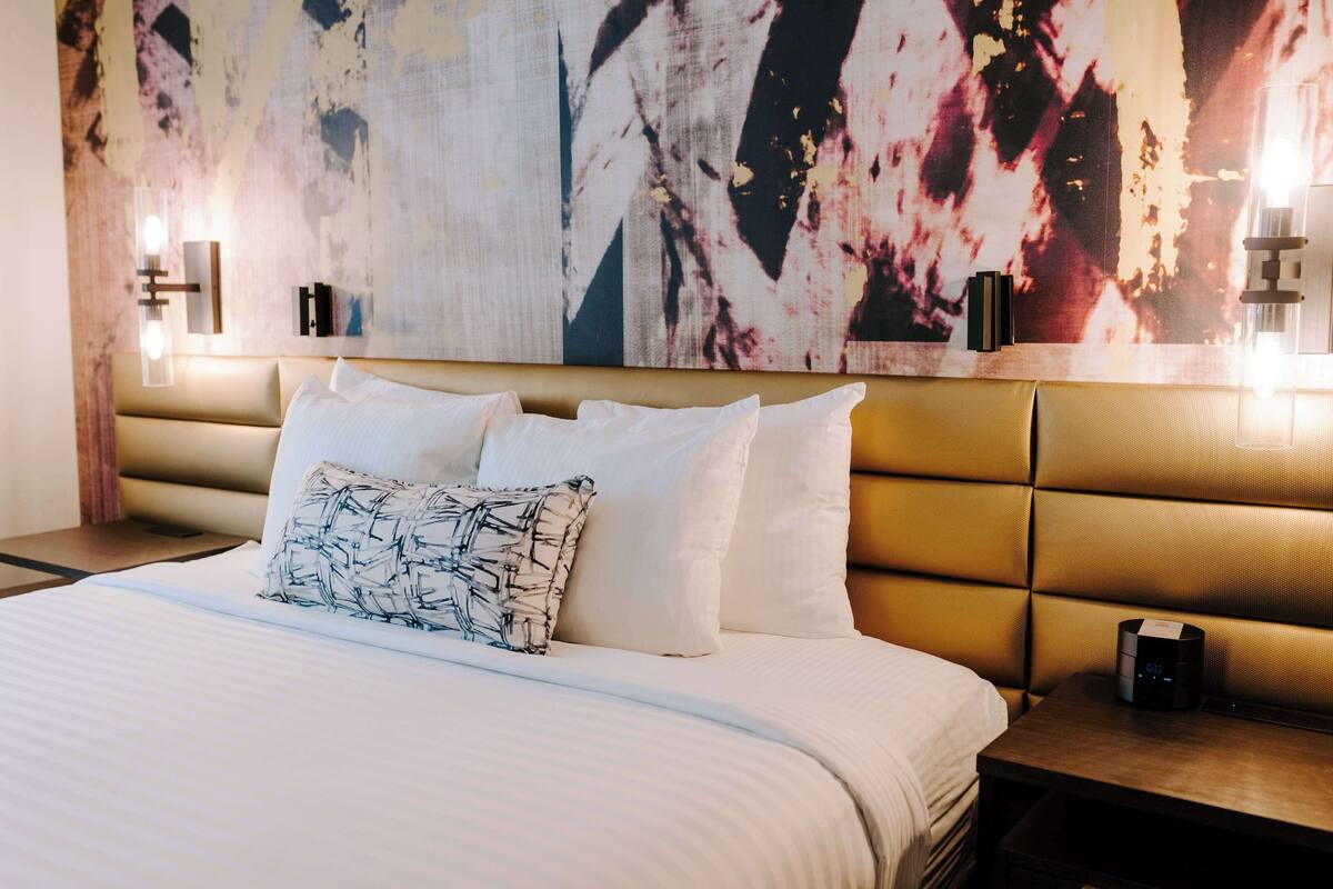 Une chambre d’hôtel dotée d’un grand lit, d’une tête de lit avec éclairage intégré et d’un mur orné d’un grand tableau abstrait.