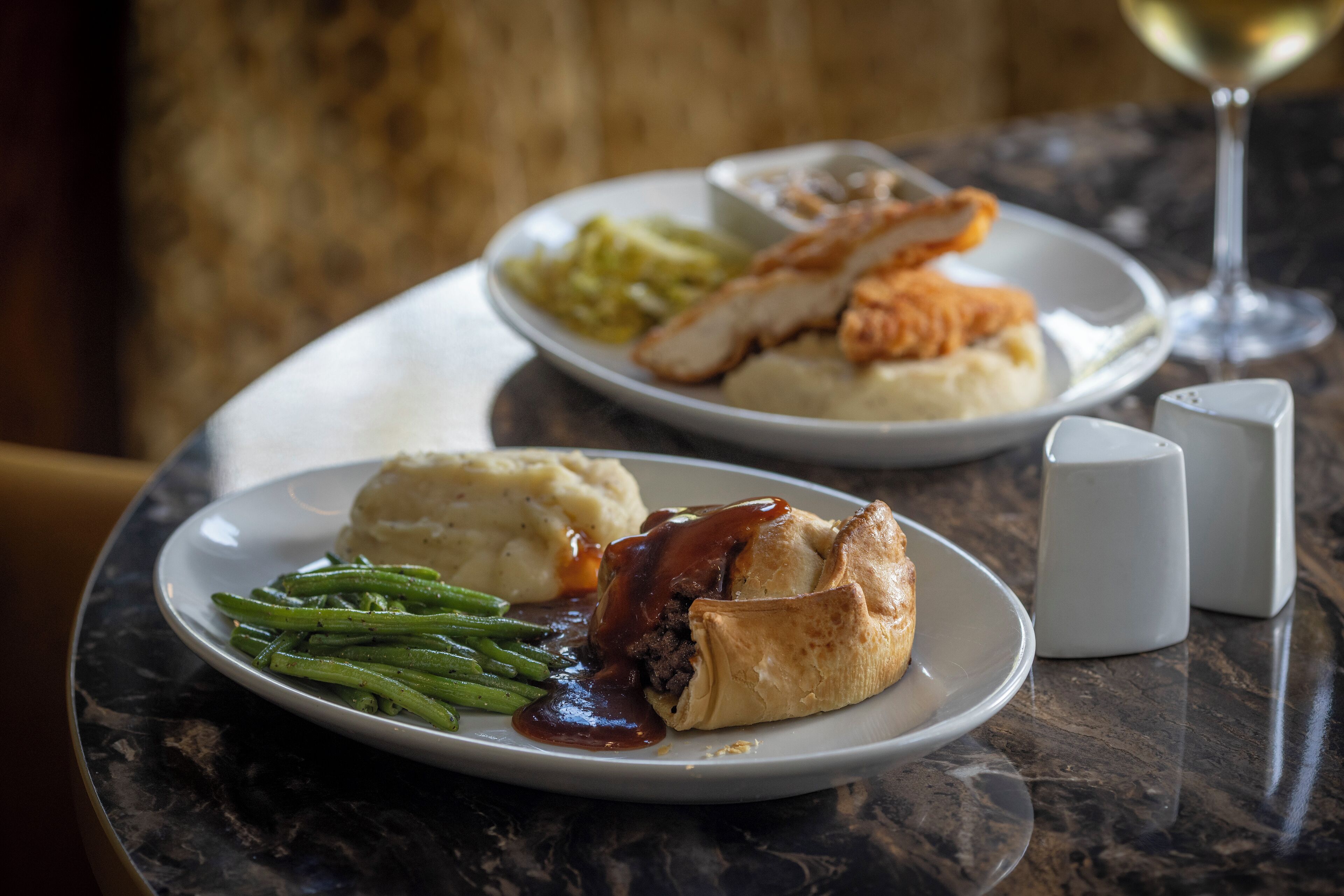 A plate of food including mashed potatoes, green beans, and a meat pie with gravy, served on a marble table.