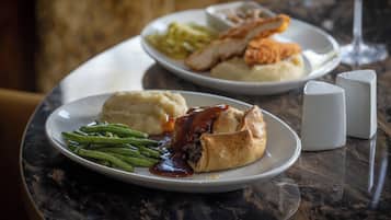 A plate of food including mashed potatoes, green beans, and a meat pie with gravy, served on a marble table.