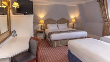 Ein Hotelzimmer mit einem Bett, zwei Nachttischen, einem Fernseher, einem Schreibtisch mit Stuhl und einem gemusterten Teppich.