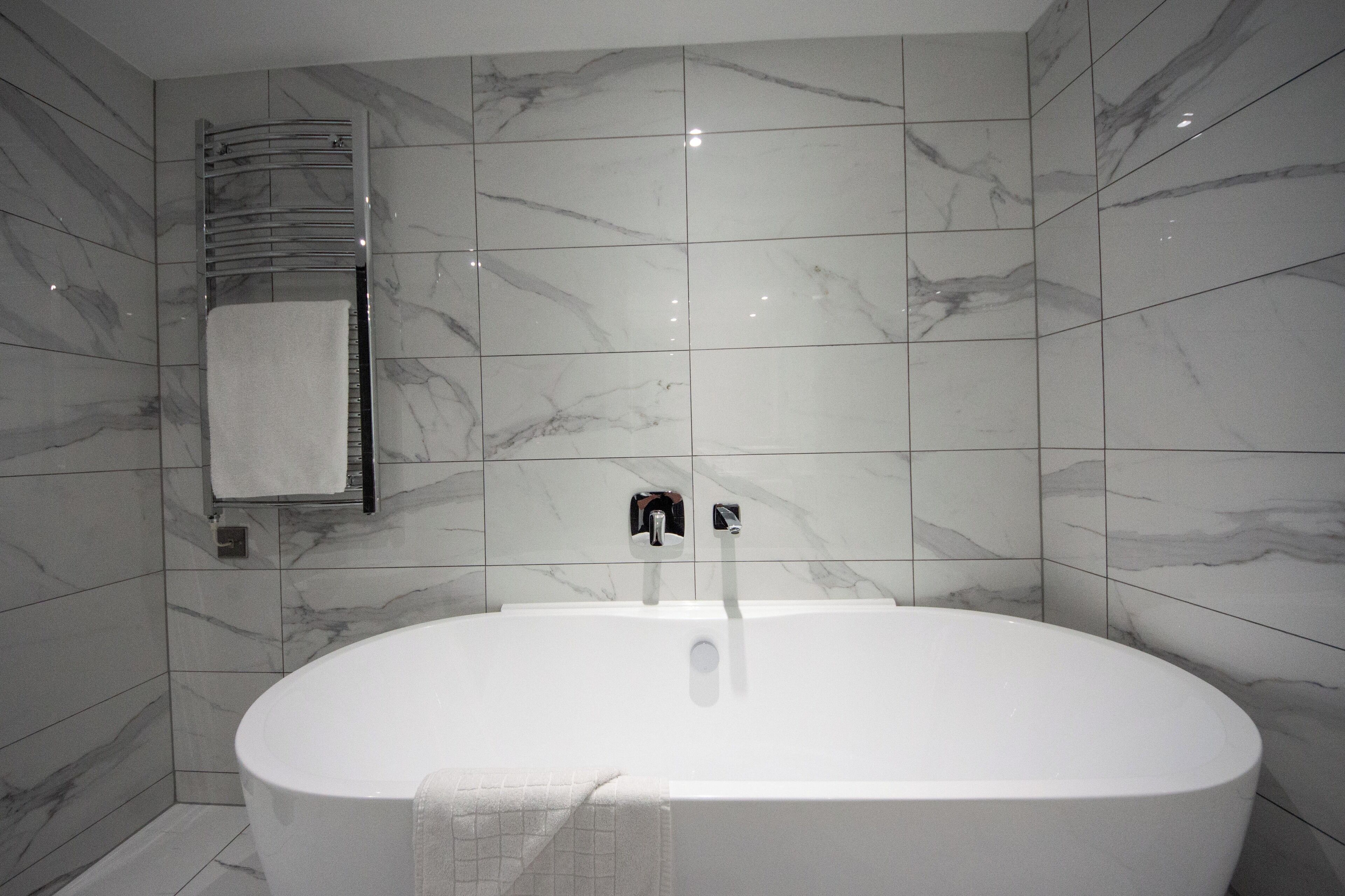 Une salle de bain moderne avec une baignoire sur pieds, un porte-serviettes et un sèche-serviettes fixé au mur.