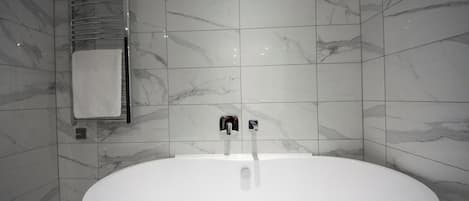 A modern bathroom with a freestanding bathtub, a towel rack, and a wall-mounted towel warmer.