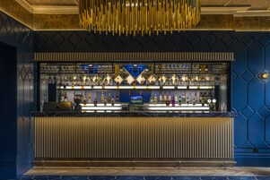 A bar area with a counter, shelves of bottles, and a television screen.