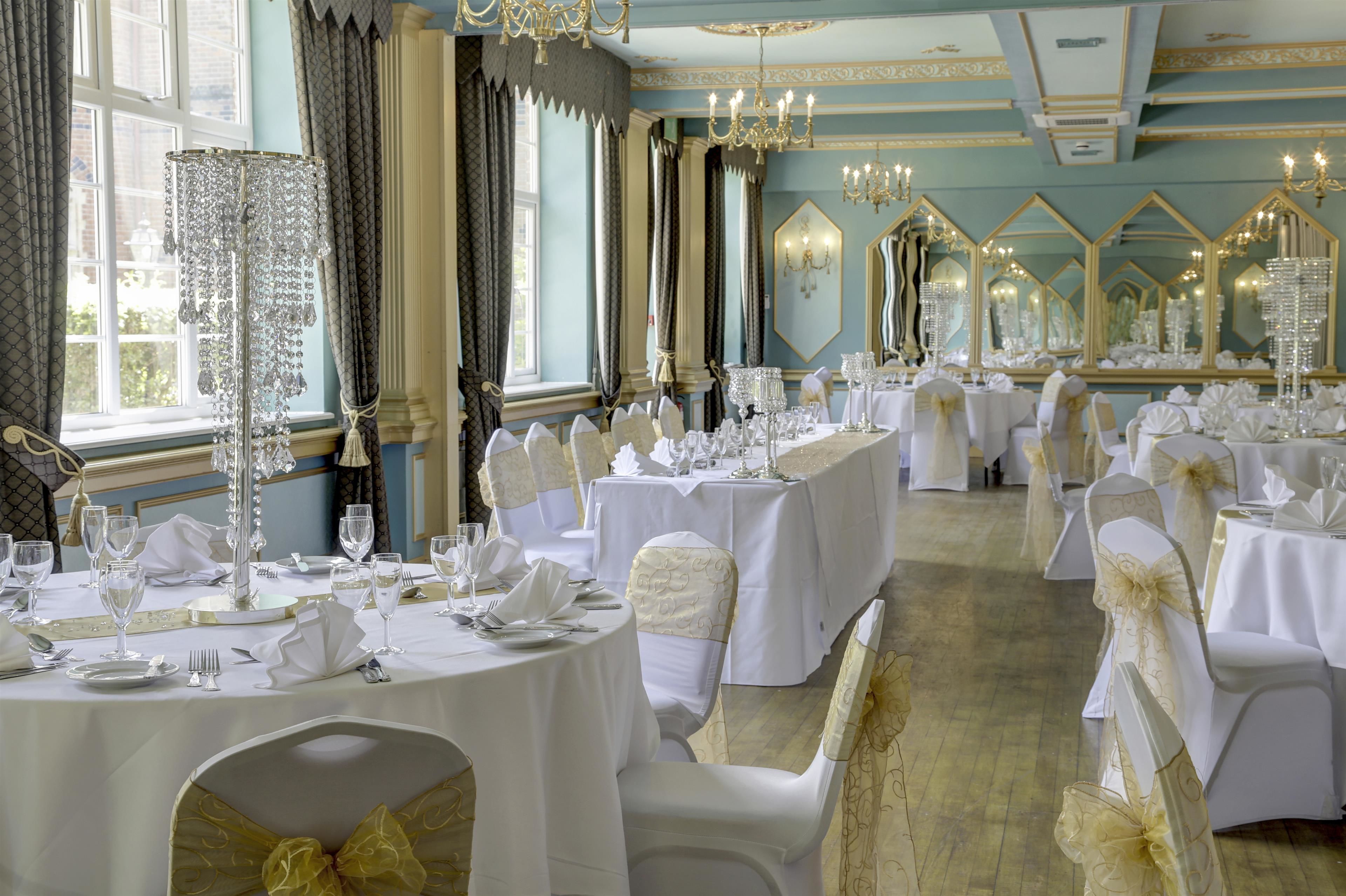 A banquet hall with round tables, white tablecloths, and gold chair sashes.