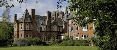 A large, historic building with multiple chimneys and arched windows, surrounded by a well-maintained lawn and trees.