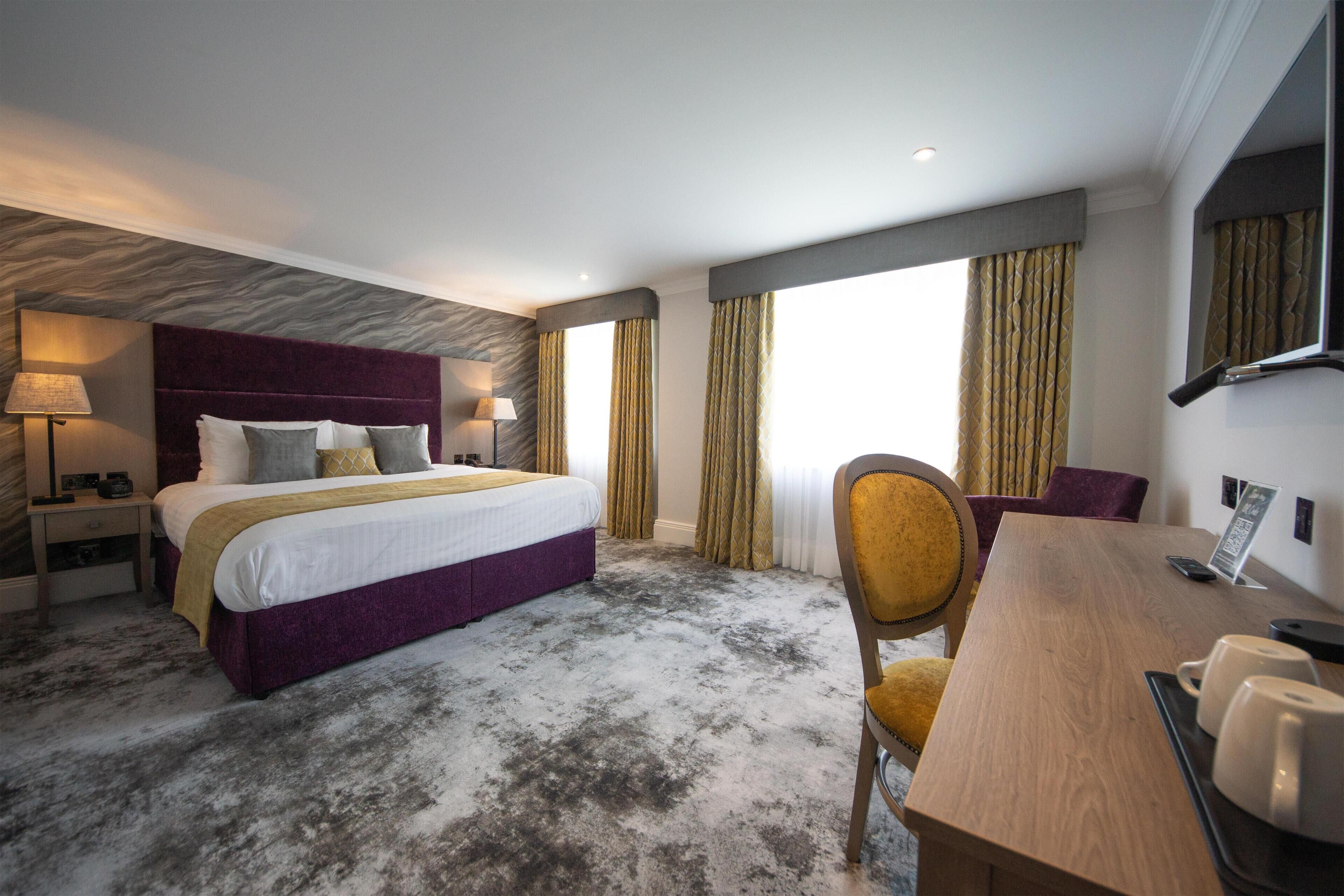 A hotel room with a large bed, a desk, a chair, and a view of the city.