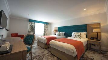 Habitación de hotel con dos camas, un escritorio con silla, televisión y ventana con cortinas.