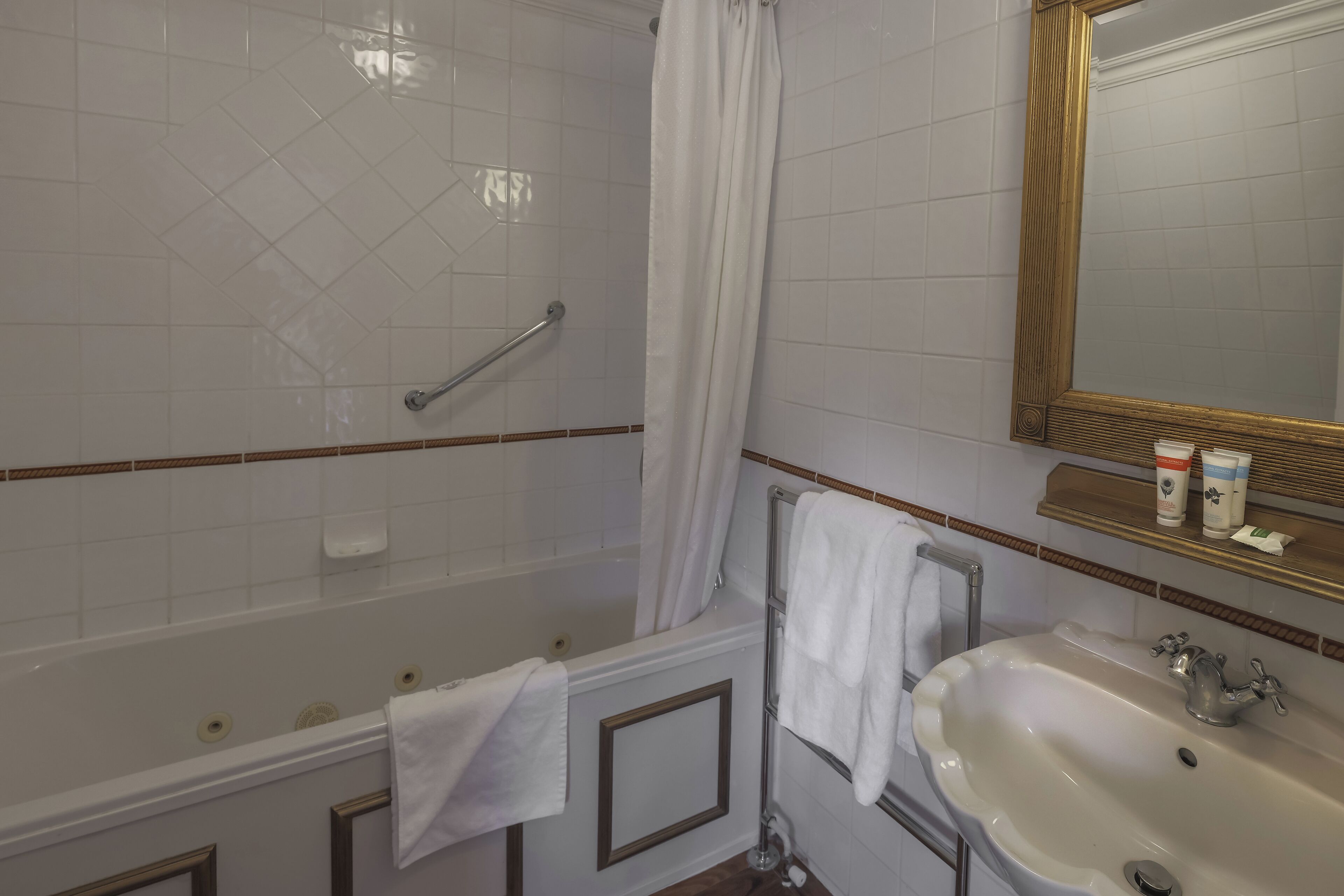 A bathroom with a bathtub, a sink, a shower with a glass door, and a mirror with a gold frame.
