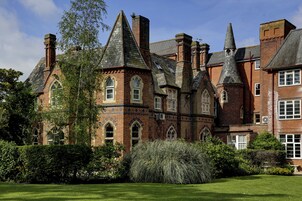 Un edificio grande e histórico con múltiples torres y ventanas de arco, rodeado de jardines bien cuidados.