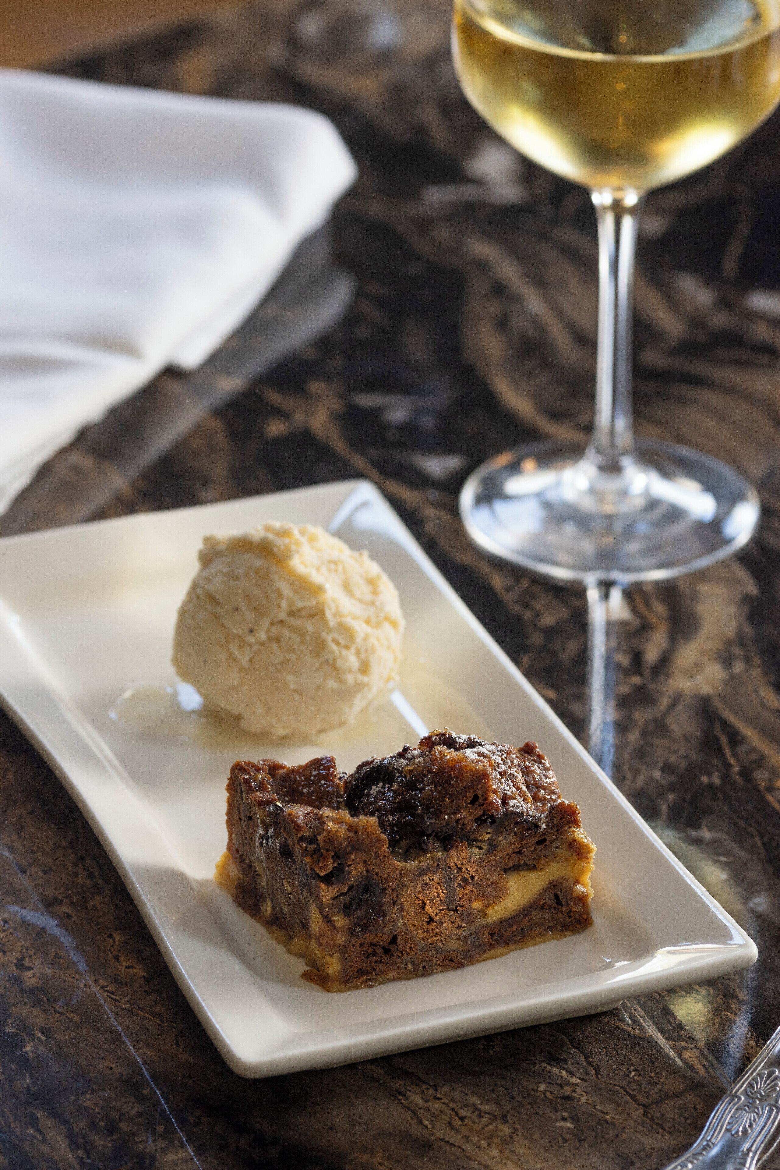 Un plato de postre con una porción de pastel y una bola de helado sobre una mesa de mármol.