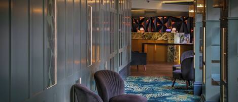 A hallway with a patterned carpet, two purple armchairs, a small round table, and a bar area with a counter and chairs.