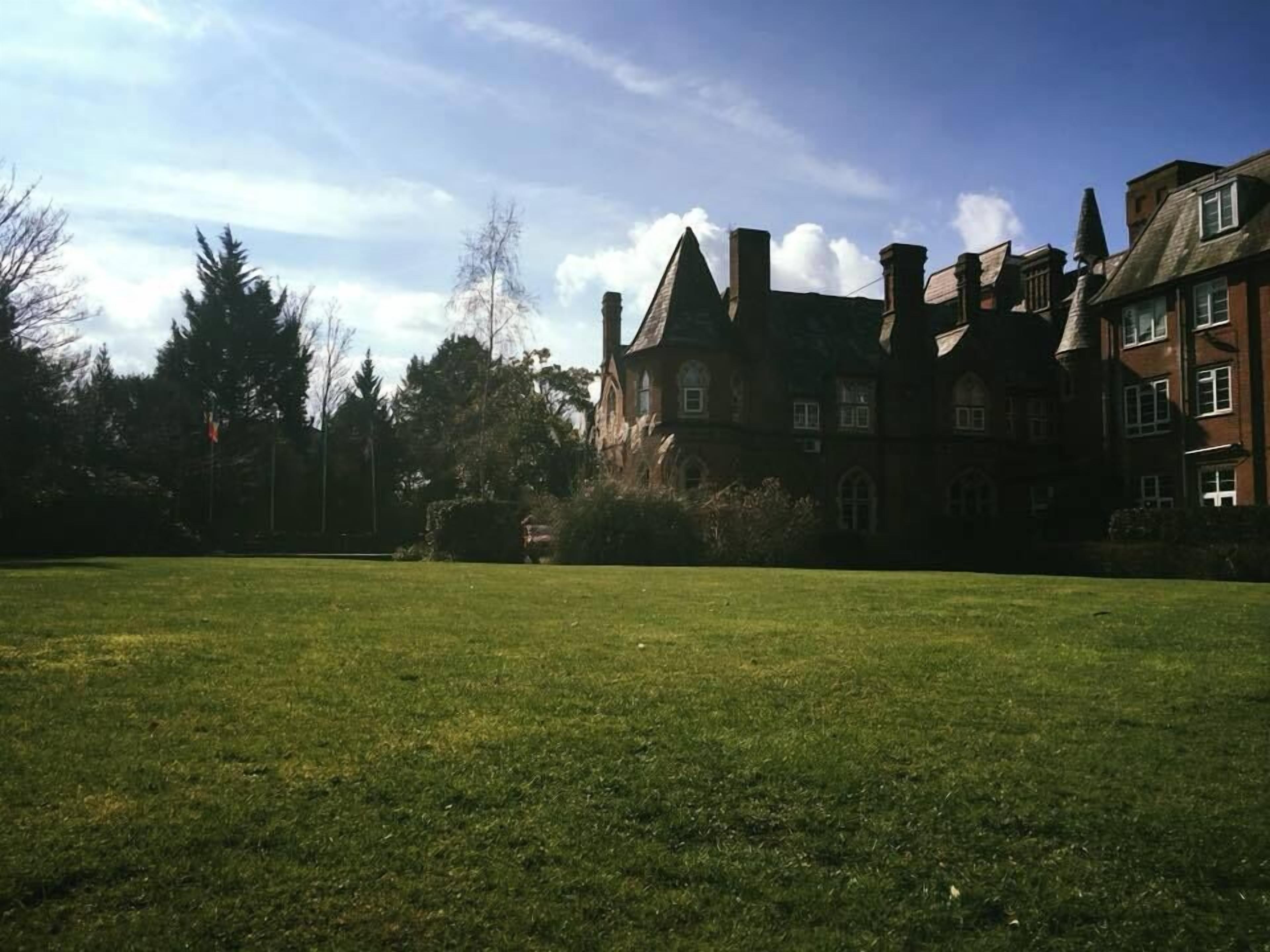 Un edificio grande e histórico con varias chimeneas y un césped bien cuidado al frente.