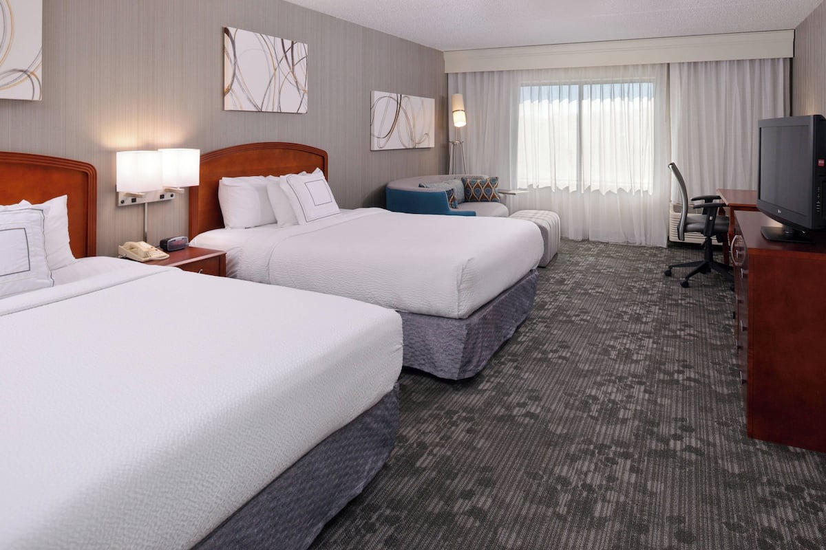 A hotel room with two beds, a desk with a television, and a chair.
