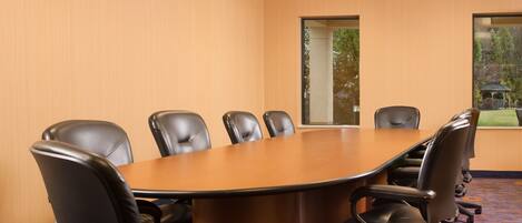 A conference room with a large oval table, six black leather chairs, and a view of a garden through a window.