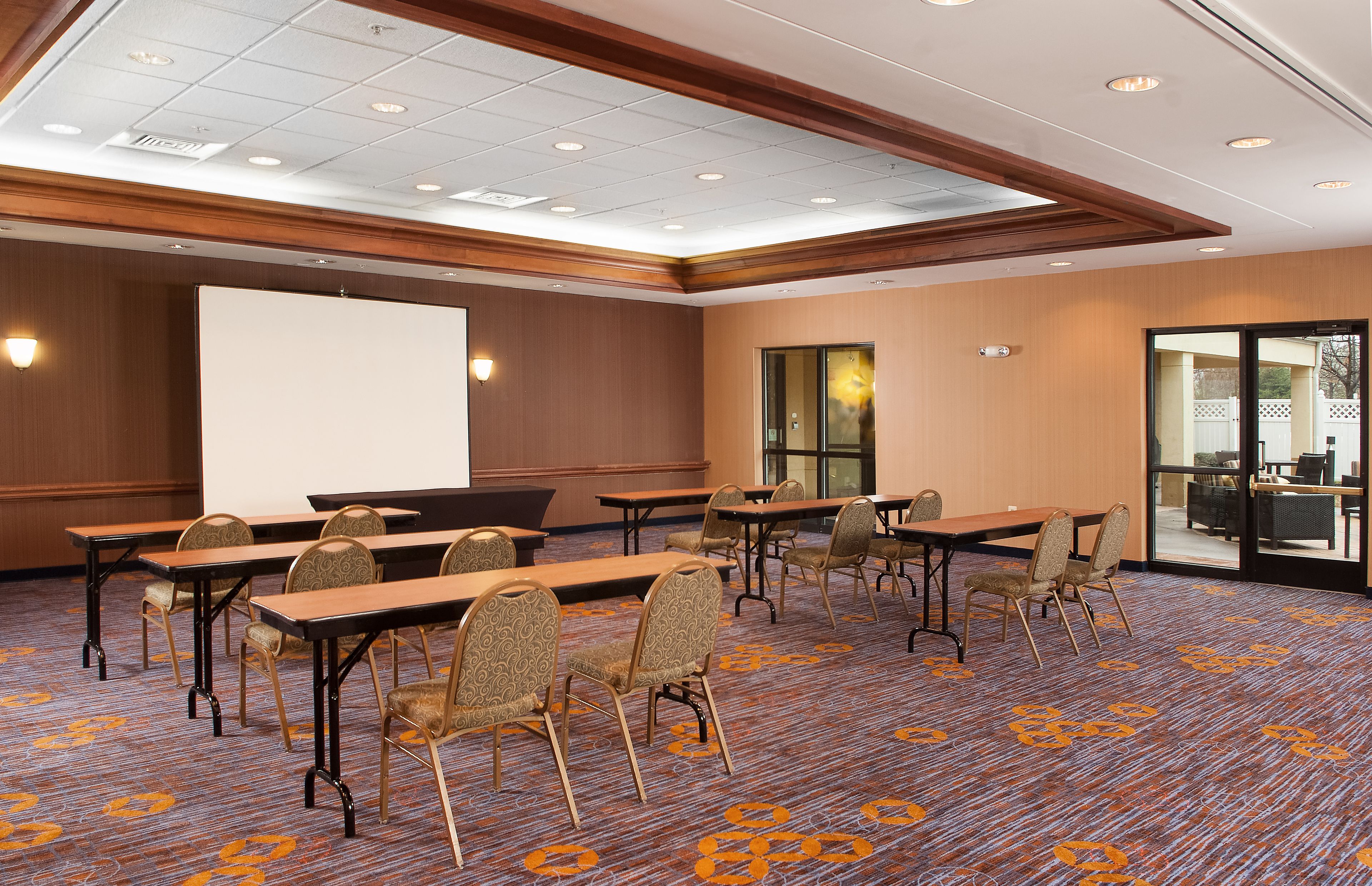 A conference room with a large screen, multiple tables, and chairs.