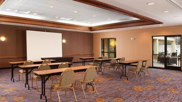 A conference room with a large screen, multiple tables, and chairs.