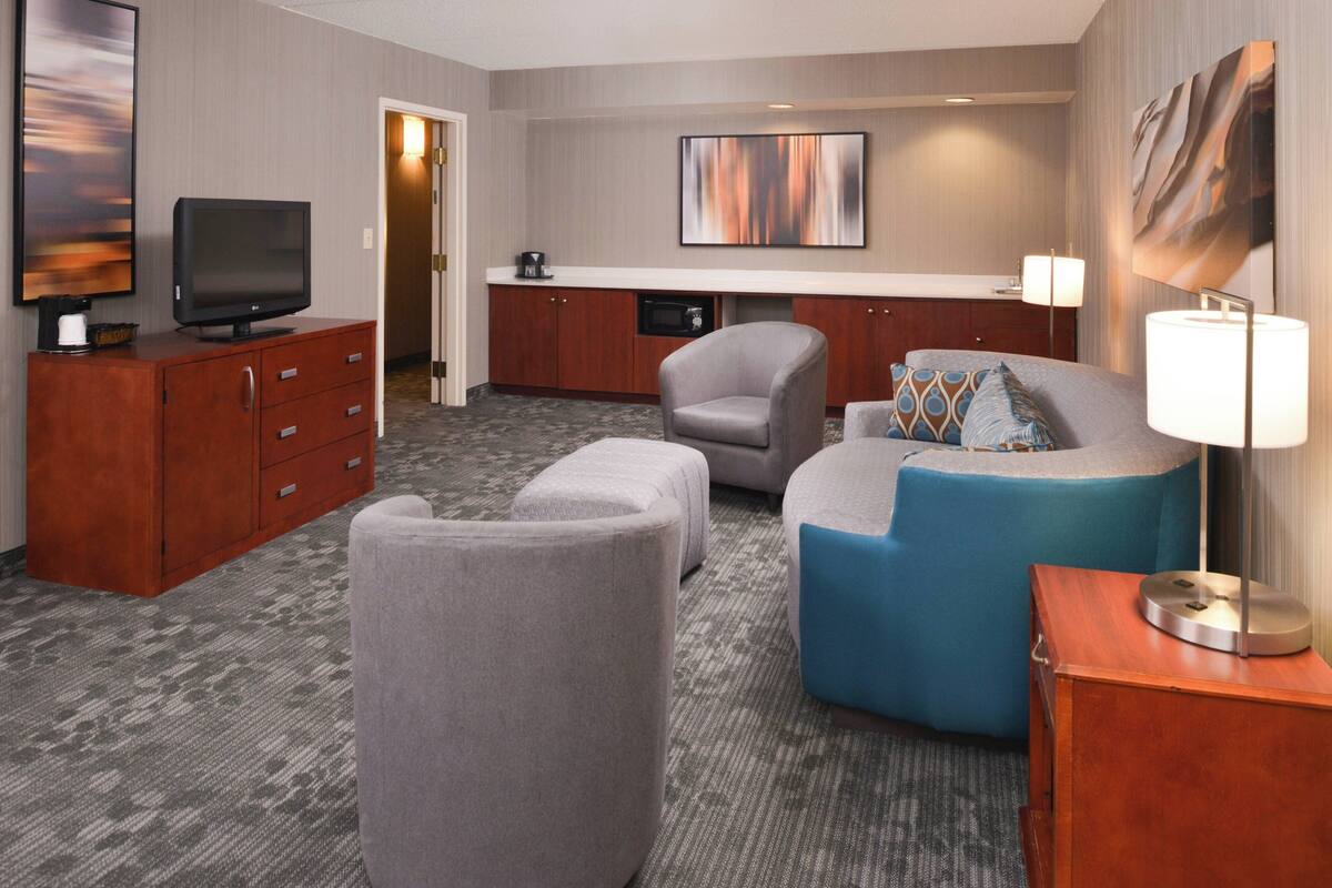 A hotel room with a flat-screen TV, a sofa, a chair, a small table, and a lamp.