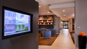 A modern hotel lobby with a digital display, comfortable seating, and a carpeted floor.