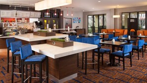 A modern restaurant with a bar area, blue and orange seating, and a large window offering a view of the outdoors.