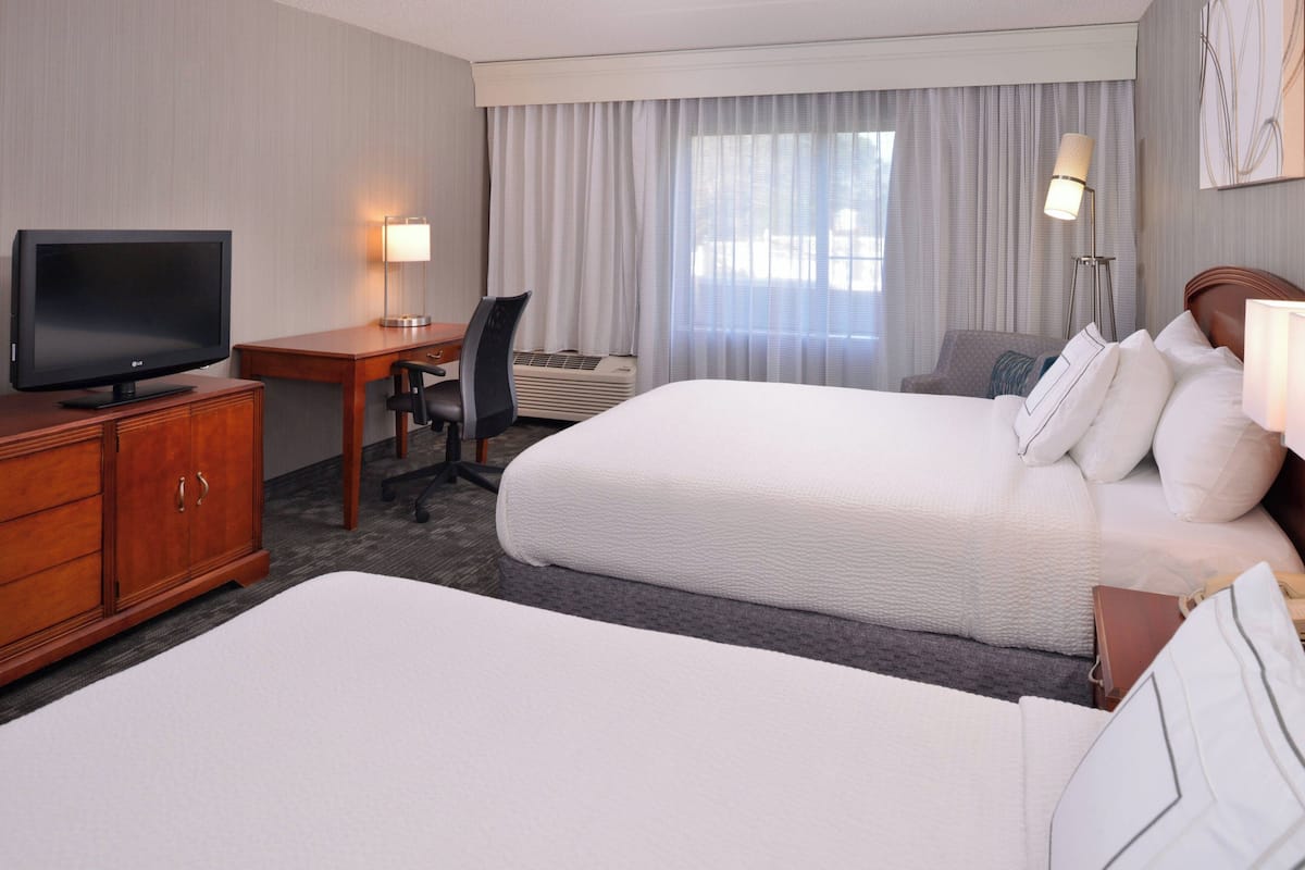A hotel room with two beds, a desk, a television, and a lamp.