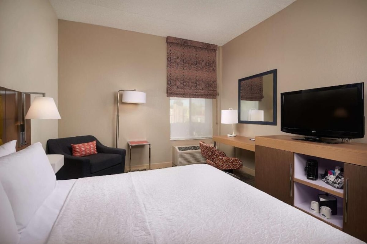 A hotel room with a bed, a television, a desk, a chair, and a lamp.