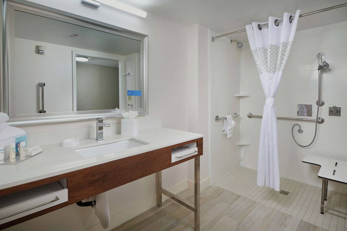 A modern bathroom with a large mirror, a sink, a shower with a curtain, and a toilet.