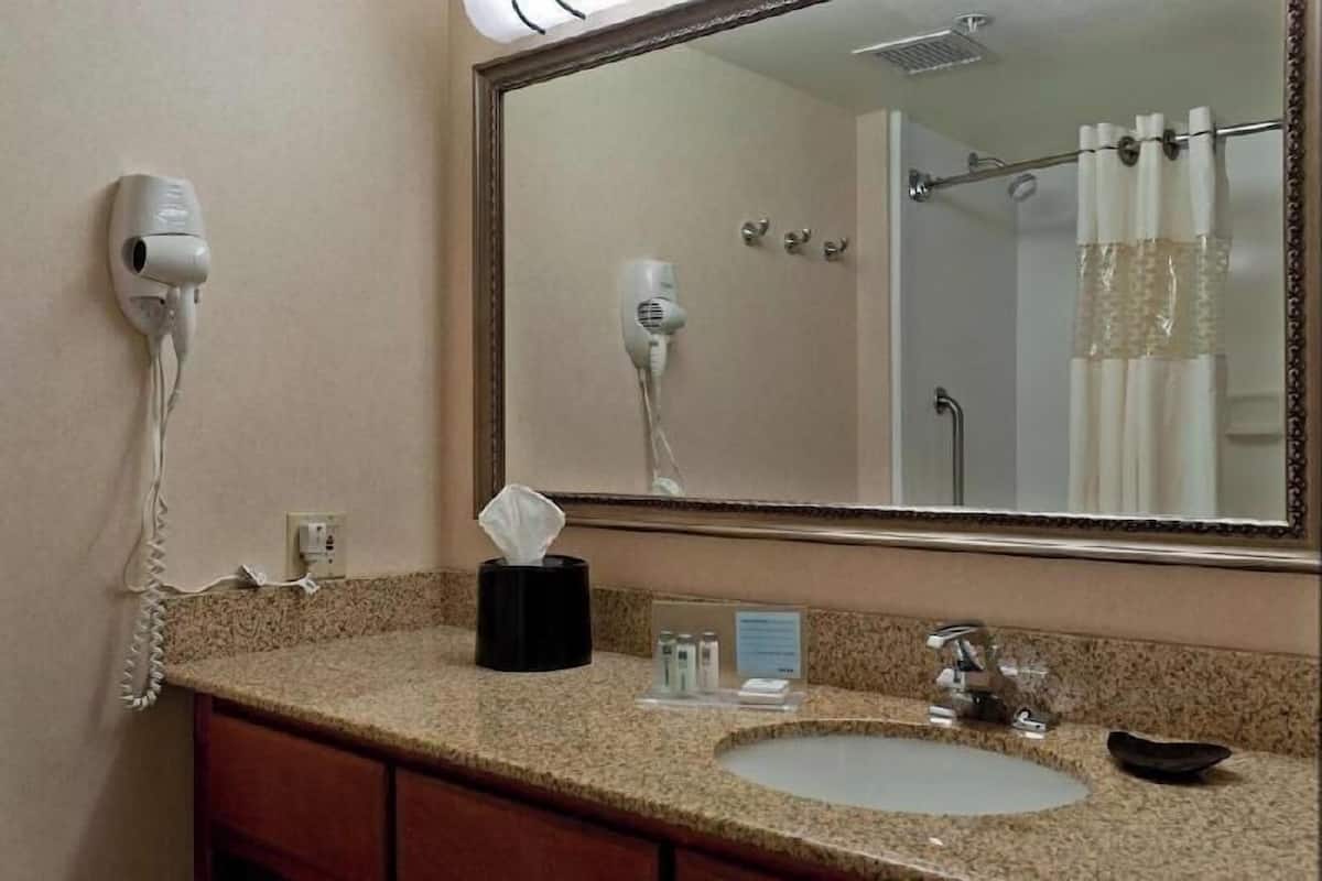 A bathroom with a sink, mirror, hair dryer, and towel dispenser.