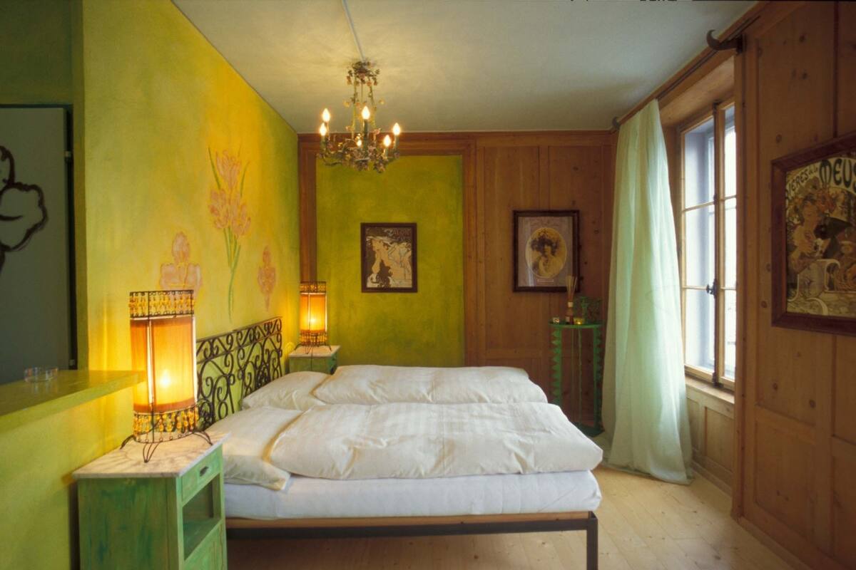 A bedroom with a bed, a chandelier, and a window with curtains.