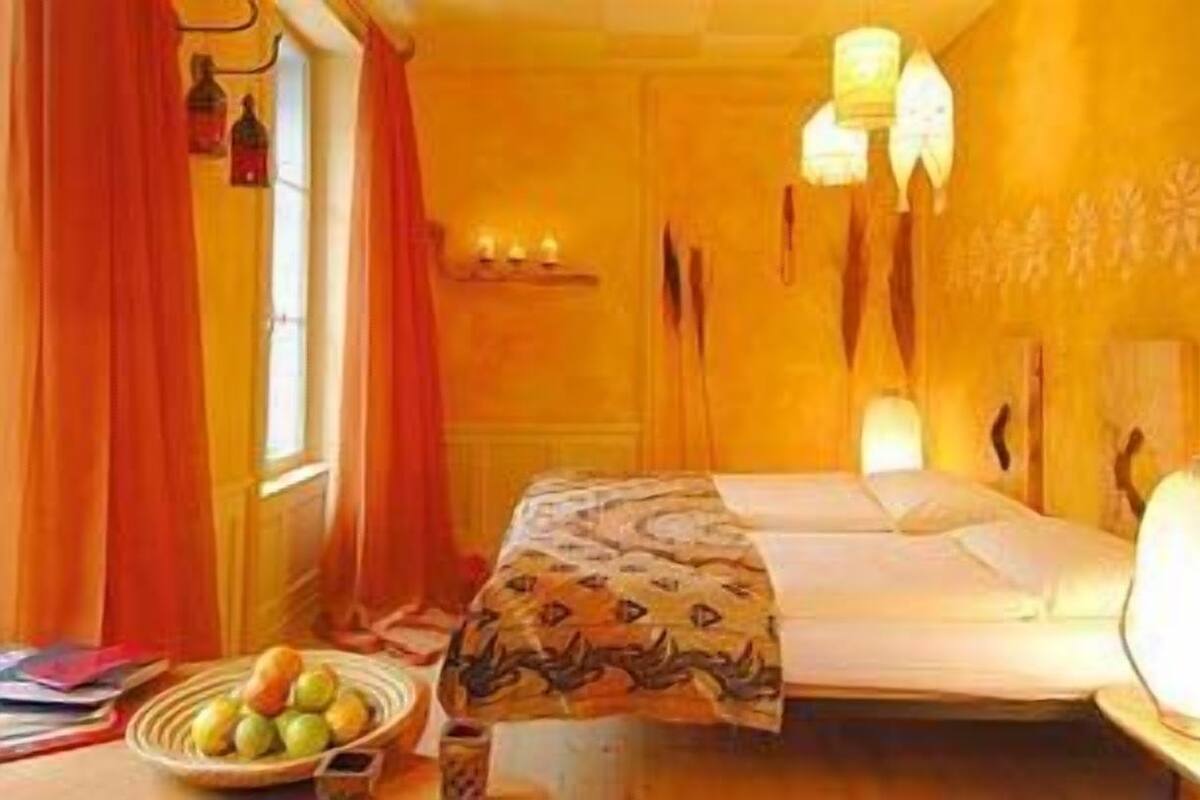 A room with a bed, a bedside table with a lamp, and a window with curtains.