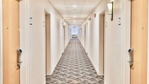 A hotel hallway with carpeted floors, wooden doors, and wall-mounted light fixtures. - Baymont by Wyndham Tucson Airport (Tucson)