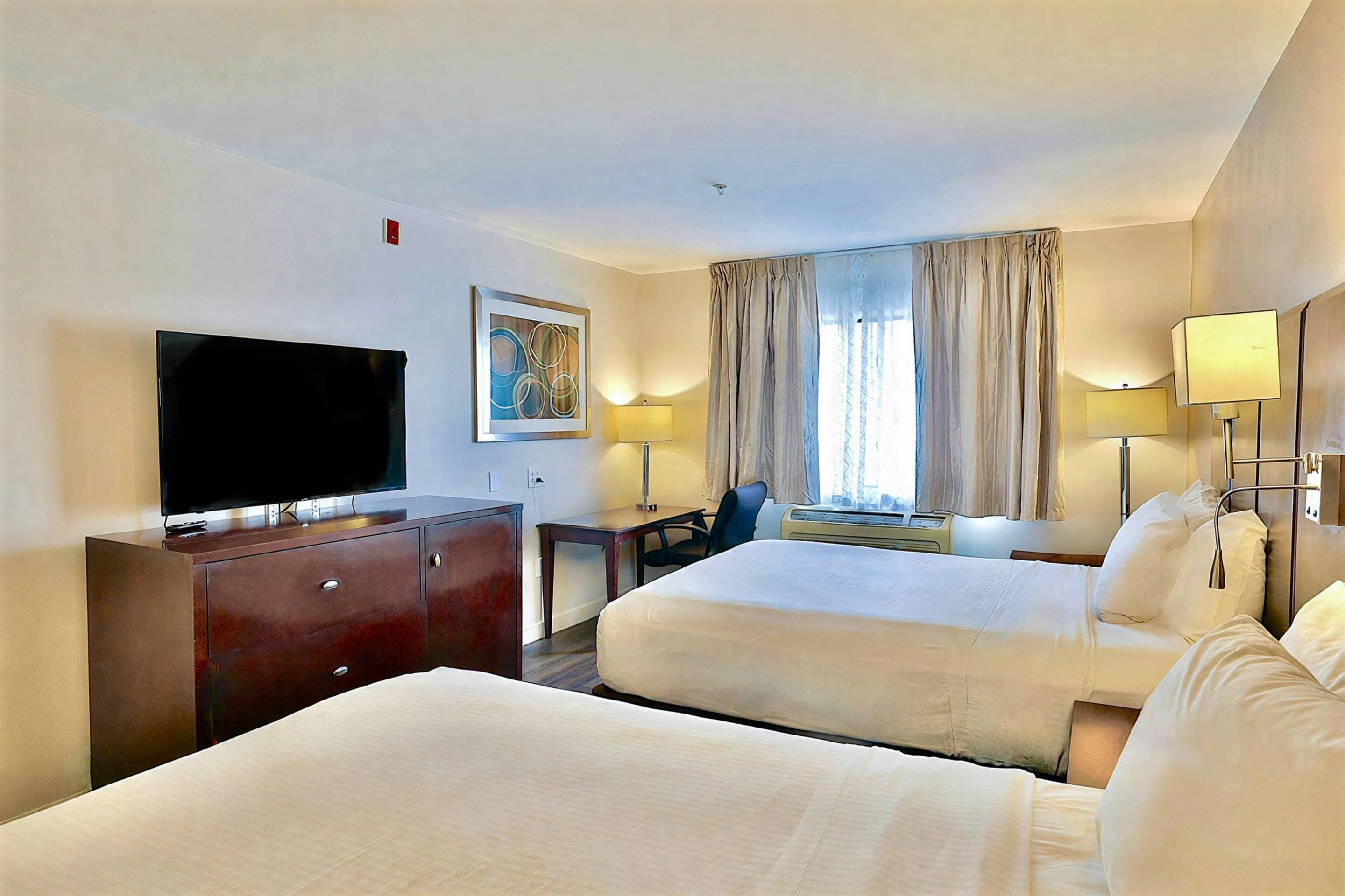 Una habitación de hotel con dos camas, televisión, escritorio y una silla.