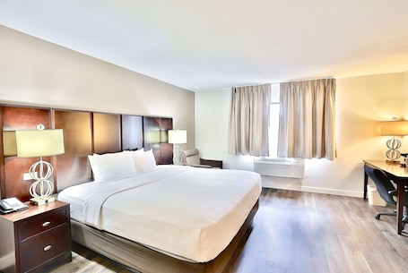 A hotel room with a large bed, bedside tables with lamps, a desk, and a window with curtains.. Baymont by Wyndham Tucson Airport
