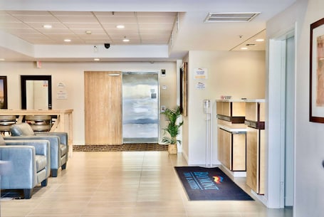 A hotel lobby with a reception desk, seating area, and a large window with a view of the sky.. Baymont by Wyndham Tucson Airport