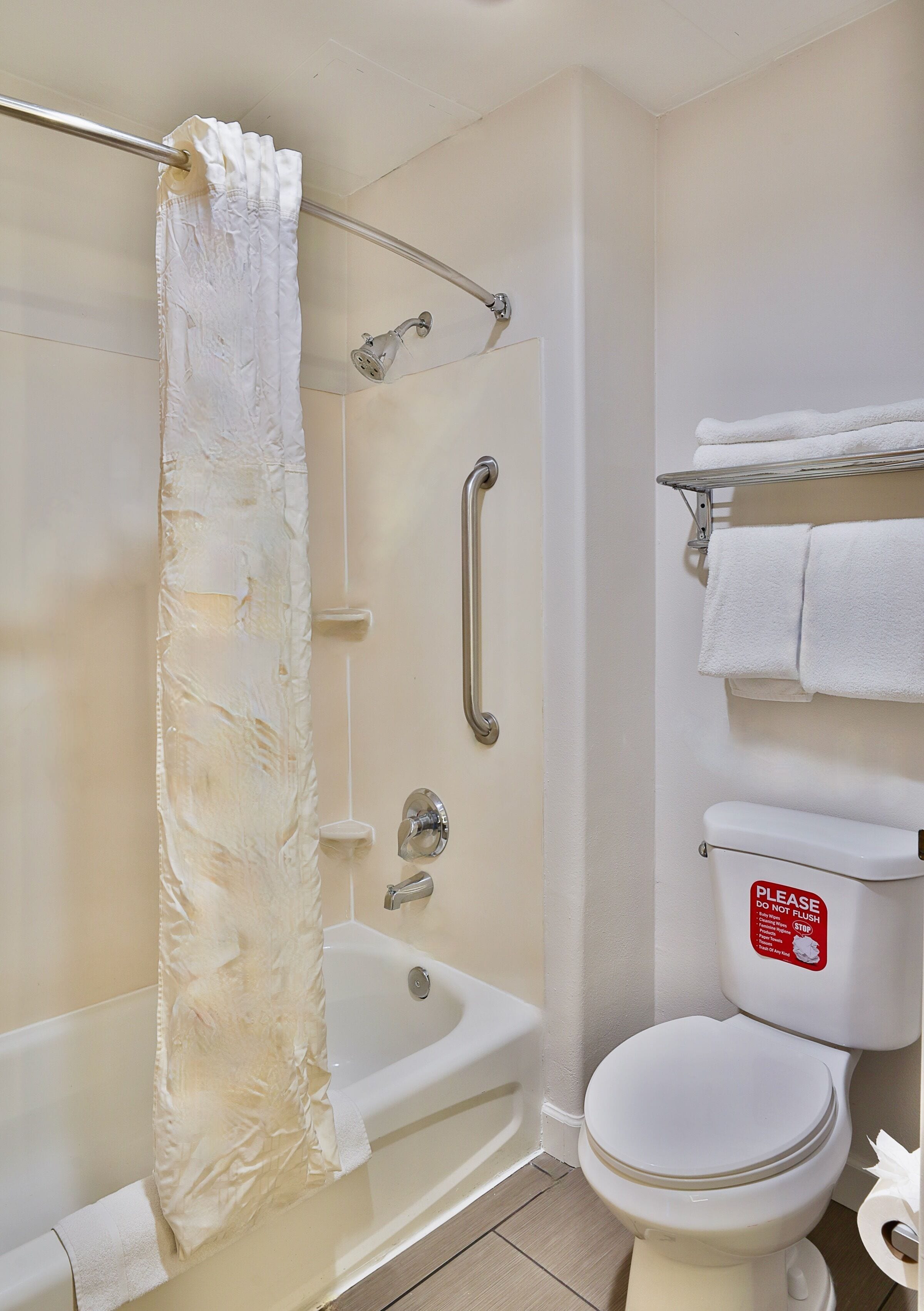 Un baño con bañera, ducha e inodoro. Hay un perchero con toallas y un cartel en el inodoro.