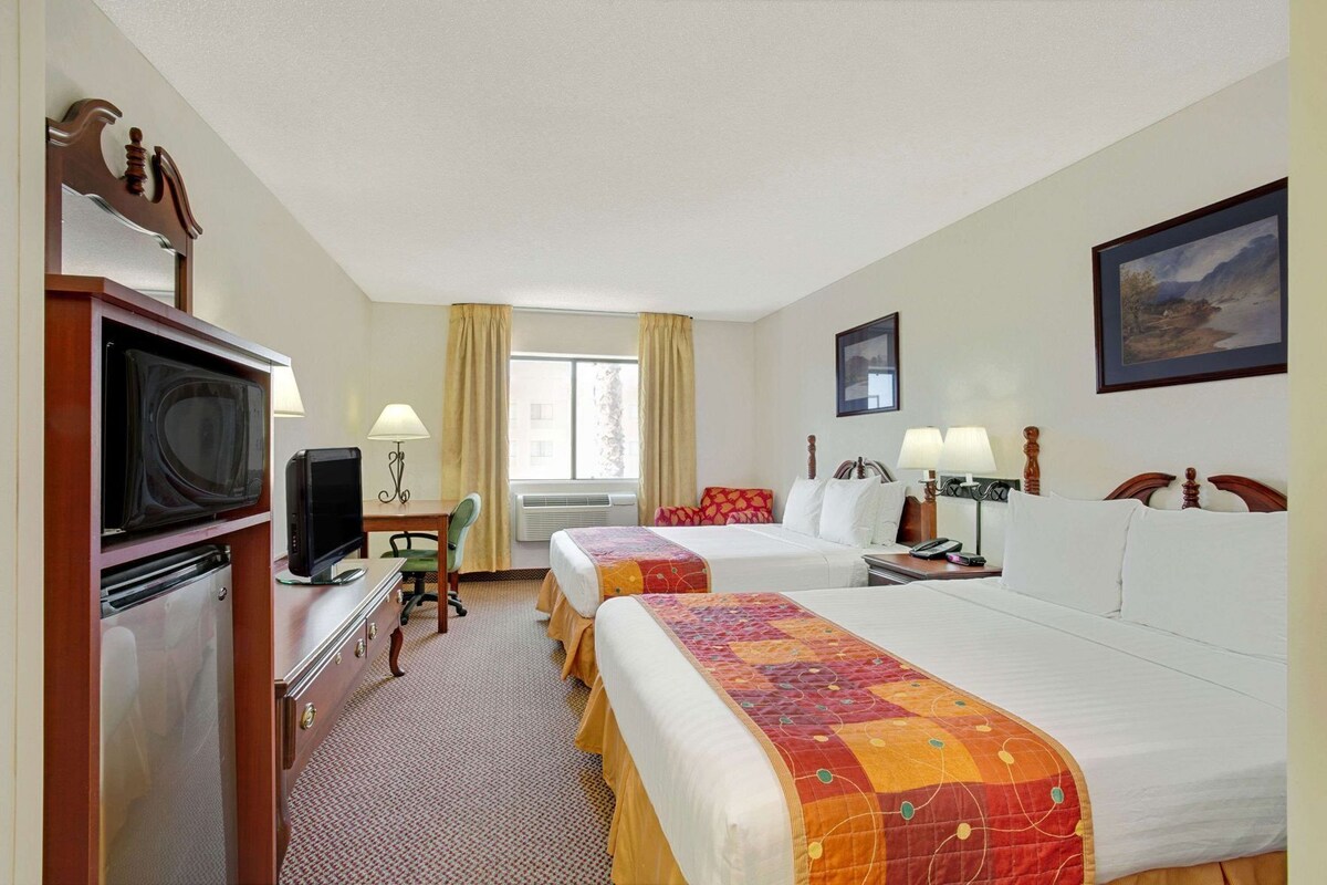 A hotel room with two beds, a desk with a TV, a microwave, and a small refrigerator.