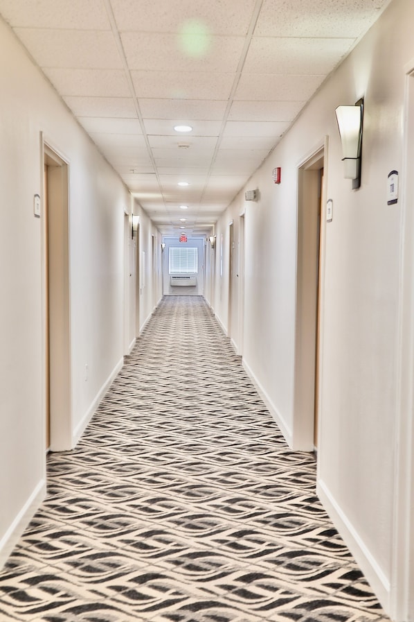 Passadís d'hotel amb una catifes estampada, portes a banda i banda i un detector de fum a la paret.