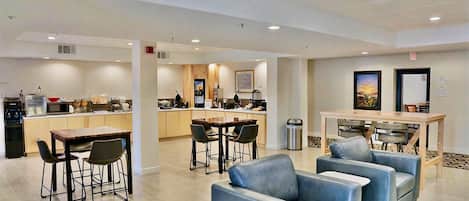 A hotel lobby with a dining area, seating, and a kitchen in the background.