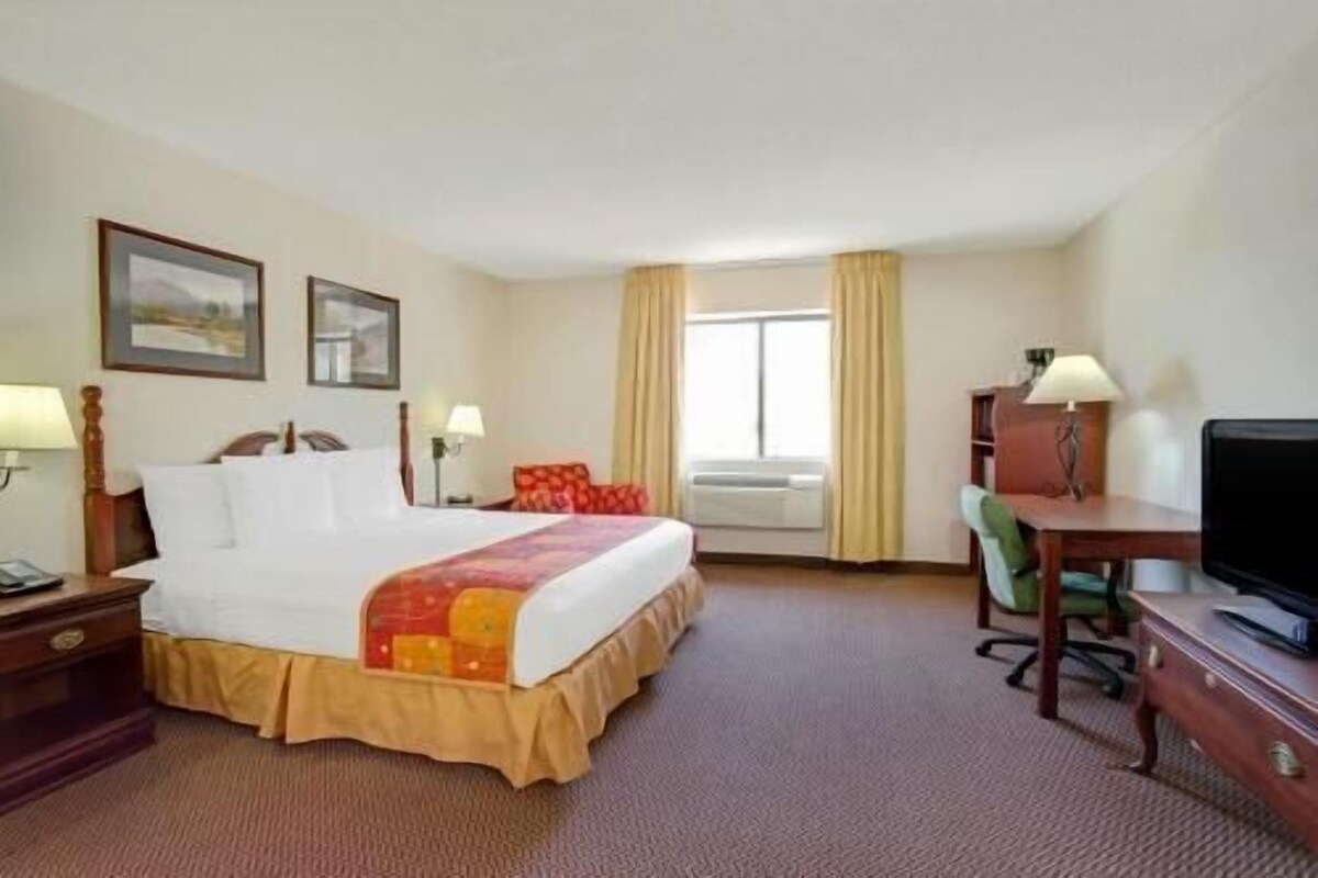 A hotel room with a bed, desk, chair, television, and air conditioning unit.
