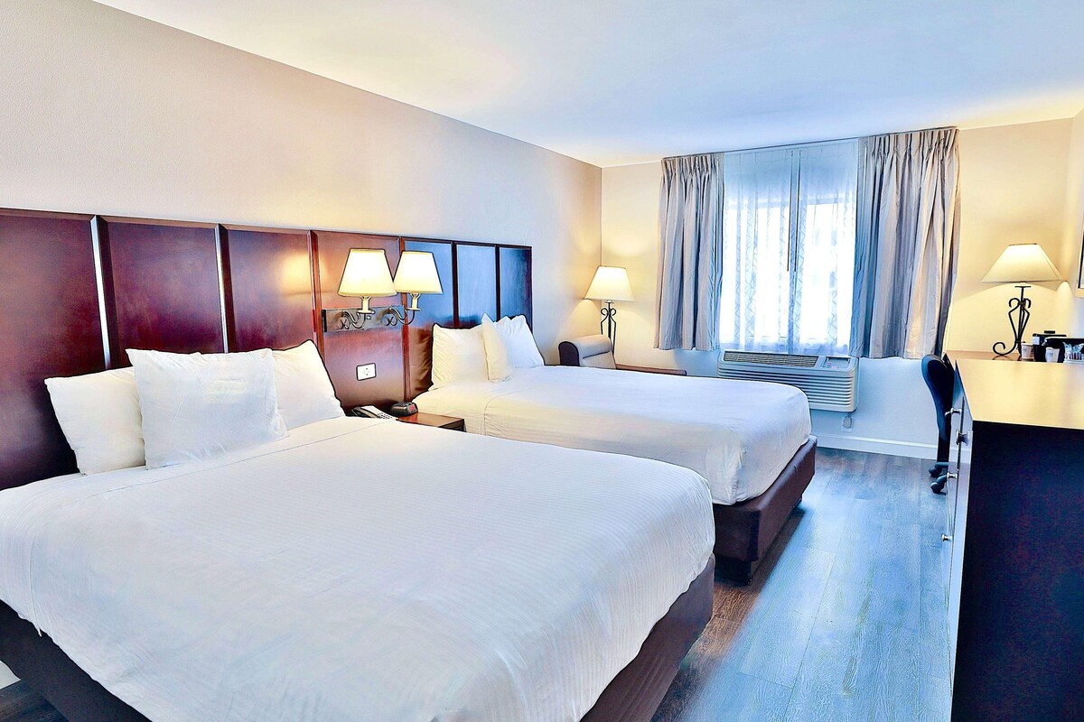 A hotel room with two beds, a desk, and a chair.