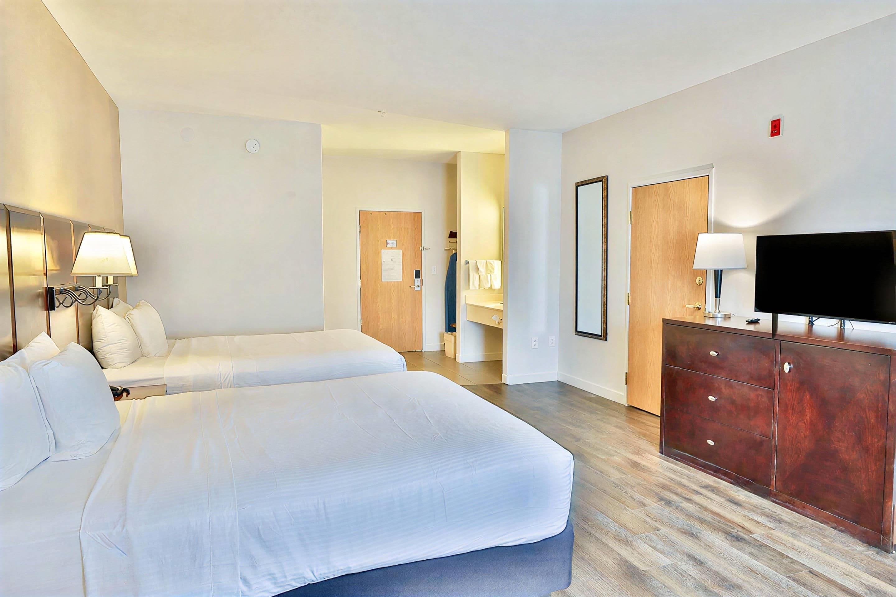 A hotel room with two beds, a TV, a dresser, and a bathroom visible in the background.