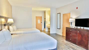 A hotel room with two beds, a TV, a dresser, and a bathroom visible in the background.