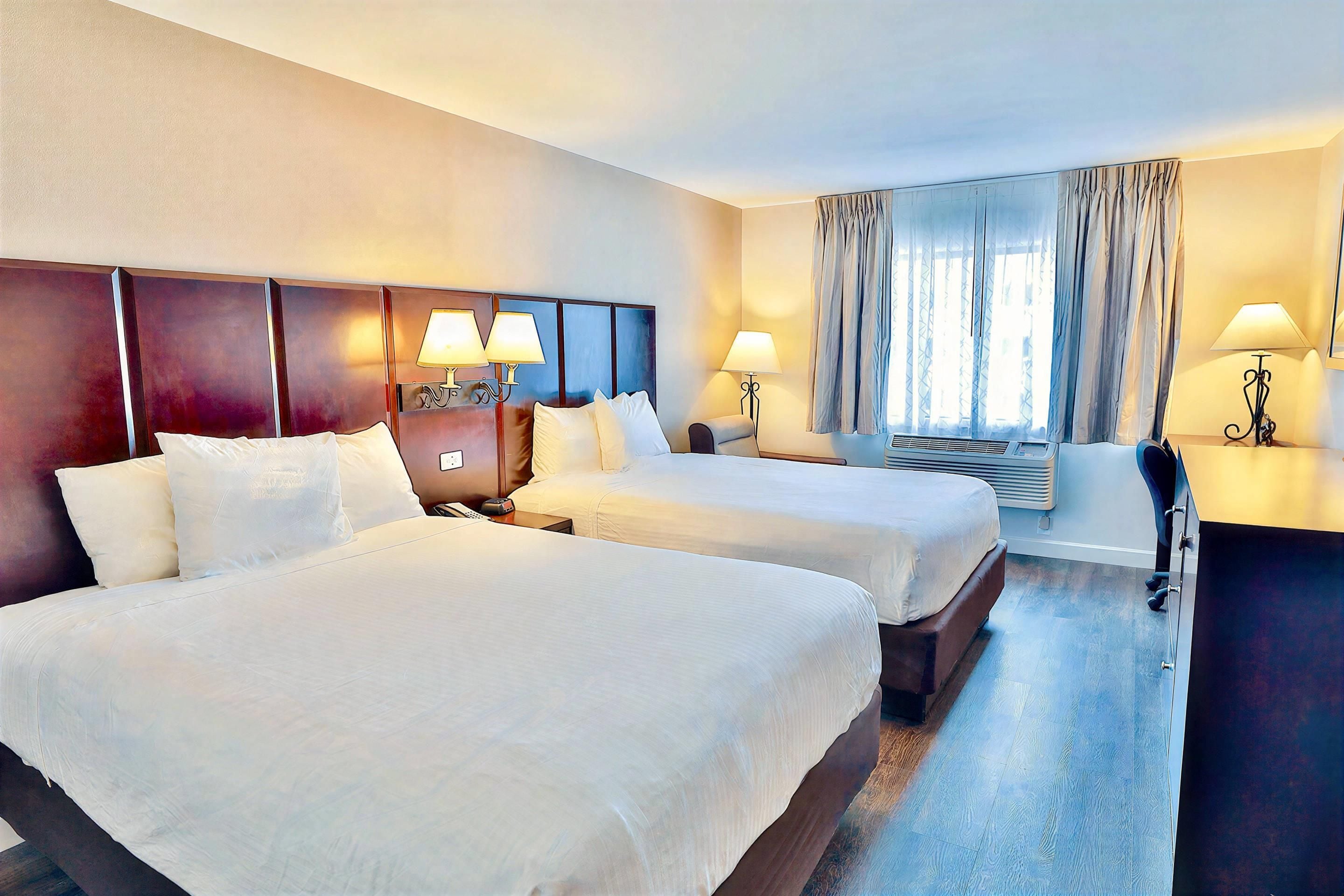 A hotel room with two beds, a desk, and a window with curtains.