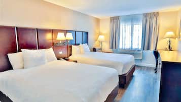 A hotel room with two beds, a desk, and a window with curtains.