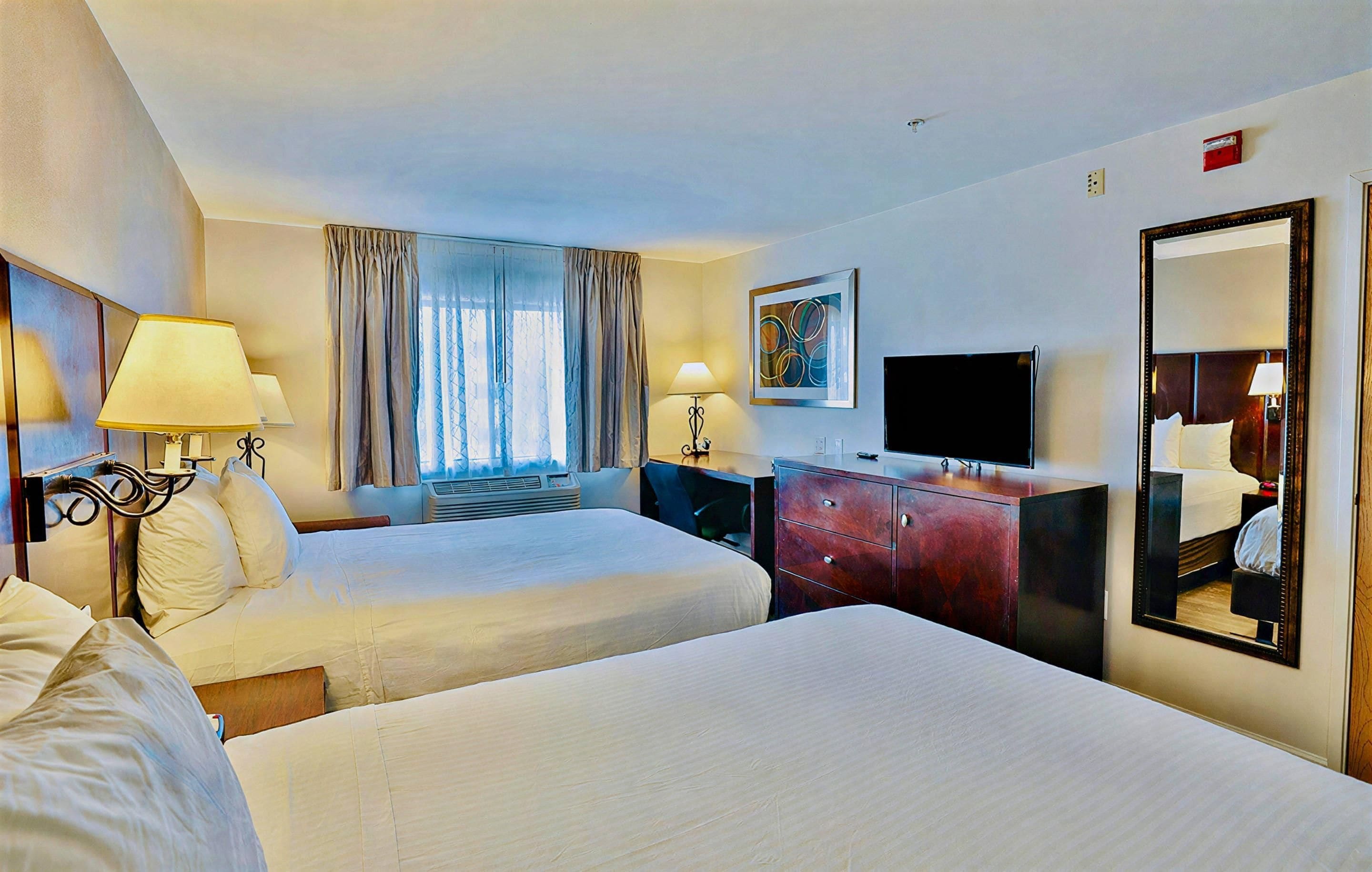 Una habitación de hotel con dos camas, televisión, cómoda y ventana con cortinas.